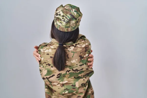 Young south asian woman wearing camouflage army uniform hugging oneself happy and positive from backwards. self love and self care