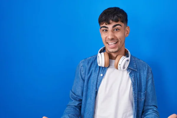 Jovem Hispânico Homem Sobre Fundo Azul Sorrindo Alegre Com Braços — Fotografia de Stock