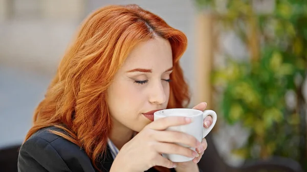 年轻的红头发女商人在咖啡店的阳台上闻到咖啡的味道 — 图库照片