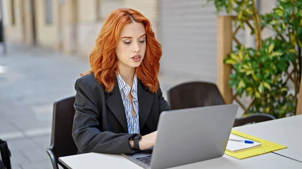 喫茶店のテラスでノートパソコンを使って働く若い赤毛の女性ビジネスワーカー — ストック写真
