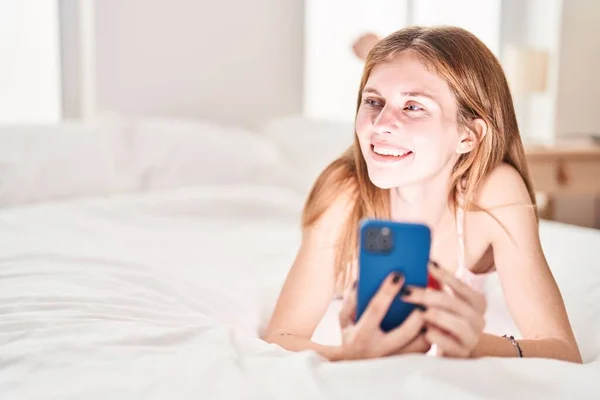 Yatak Odasında Uzanmış Akıllı Telefon Kullanan Genç Sarışın Kadın — Stok fotoğraf