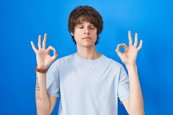 站在蓝色背景上的西班牙裔年轻人放松了 闭上眼睛 用手指做冥想动作 瑜伽概念 — 图库照片