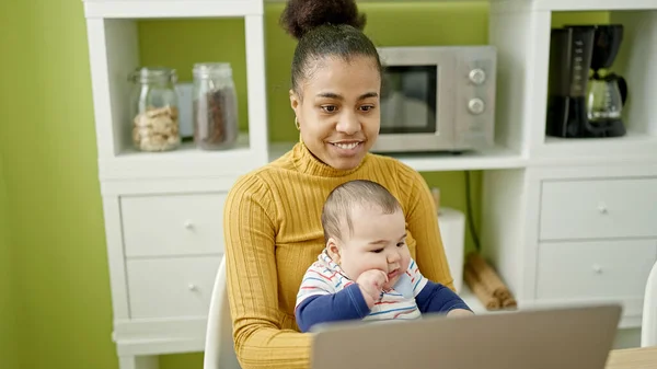 母親と息子はオンラインで働いているテーブルの上に座っている間ケア赤ちゃんはダイニングルームで — ストック写真