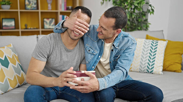Two men couple surprise with gift covering eyes at home