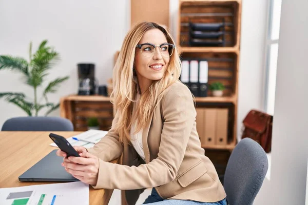Young blonde woman business worker smiling confident using smartphone at office