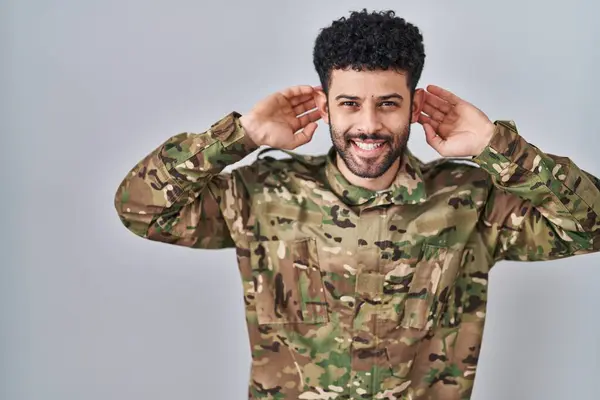 Arap Adam Kamuflaj Üniforması Giyip Gülümsüyor Parmaklarıyla Kulaklarını Çekiyor Komik — Stok fotoğraf