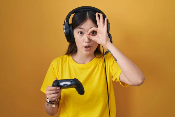 中国的年轻女子在玩电子游戏时拿着控制器做着不错的动作 脸上带着惊讶的表情 眼睛透过手指看着 不信的表情 — 图库照片