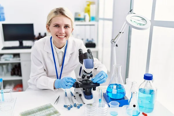 研究室で笑顔顕微鏡を使用して若いブロンド女性科学者 — ストック写真