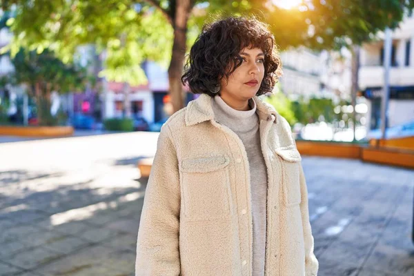 Genç, güzel, İspanyol bir kadın parkta ciddi bir ifadeyle yan tarafa bakıyor.