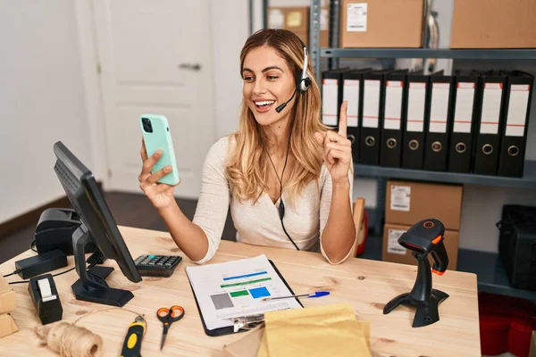 Young blonde woman working at small business ecommerce using headset smiling with an idea or question pointing finger with happy face, number one