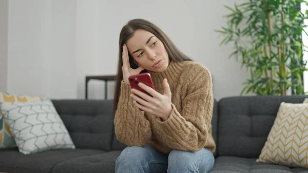 年轻美丽的惊慌失措的女人在家里用带有紧张表情的智能手机 — 图库照片