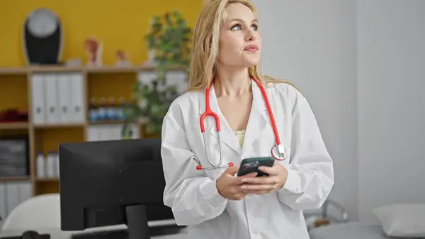 Νεαρή Ξανθιά Γυναίκα Γιατρός Χρησιμοποιώντας Smartphone Σοβαρό Πρόσωπο Στην Κλινική — Φωτογραφία Αρχείου