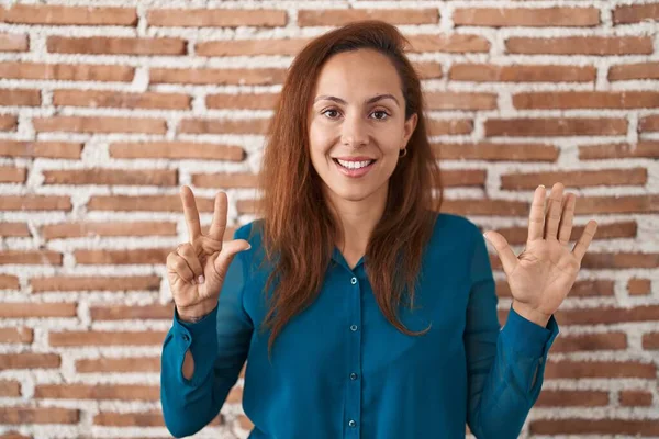 ブルネットの女性はレンガの壁の上に立って 自信と幸せに微笑んでいる間 指番号8を指で指で指摘します — ストック写真