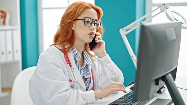 Mujer Pelirroja Joven Médico Usando Ordenador Hablando Teléfono Inteligente Clínica —  Fotos de Stock