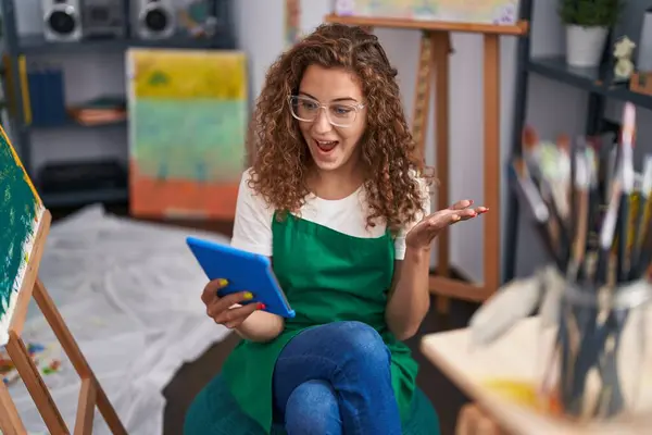 年轻的高加索女画家坐在艺术演播室里 用平板电脑进行视频通话 带着快乐的微笑和高傲的表情庆祝成就 — 图库照片