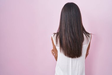 Brunette young woman standing over pink background wearing glasses standing backwards looking away with crossed arms 