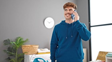 Çamaşır odasında gülümseyen akıllı telefondan konuşan genç İspanyol adam.