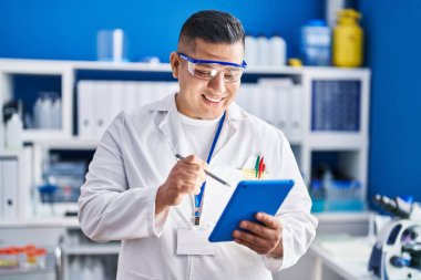 Laboratuvarda dokunmatik ped kullanarak gülümseyen genç Latin bilim adamı.