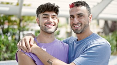 Two men couple smiling confident hugging each other at park