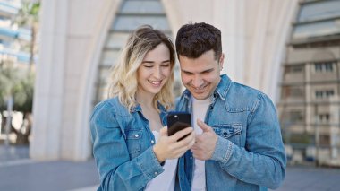 Kadın ve erkek caddede akıllı telefon kullanarak yan yana duruyorlar.