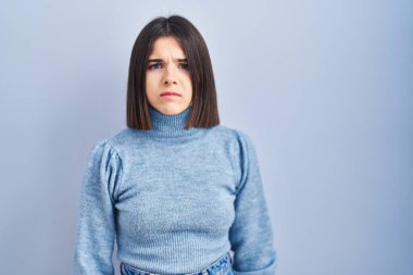 Mavi arka planda duran Latin kökenli genç bir kadın depresif ve endişeli, sinirli ve korkmuş bir şekilde ağlıyor. hüzünlü ifade. 