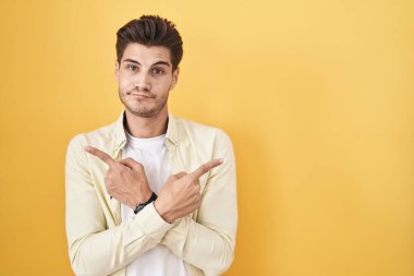 Sarı arka planda dikilen genç İspanyol adam her iki tarafı da parmaklarıyla işaret ediyor. Farklı yönler farklı. 