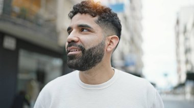 Young hispanic man smiling confident looking to the side at street
