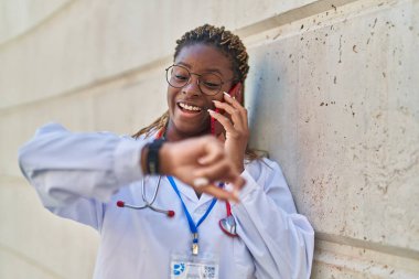 Afro-Amerikalı kadın doktor akıllı telefondan konuşuyor hastanede nöbet tutuyor.