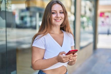 Sokakta akıllı telefon kullanan, kendine güvenen genç sarışın kadın.