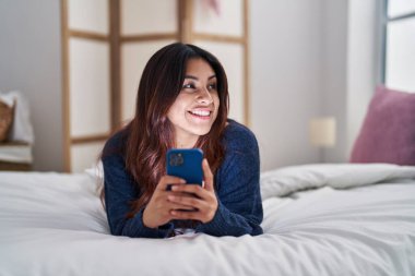 Genç İspanyol kadın yatakta akıllı telefon kullanıyor.