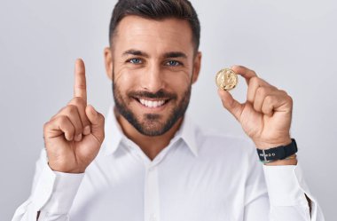 Elinde litekoin kripto para tutan yakışıklı bir adam bir fikre ya da soru işaretine şaşırmış ve mutlu bir yüzle işaret ediyor. 
