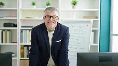 Orta yaşlı, kır saçlı, gülümseyen öğretmen üniversite sınıfında beyaz tahtada kendine güvenen.