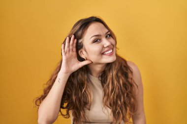 Sarı arka planda dikilmiş, ağzı kulaklarına varan gülümseyerek dedikodu ve dedikoduları dinleyen genç bir İspanyol kadın. Sağırlık kavramı. 