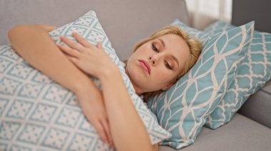 Evdeki üzgün ifadesiyle kanepede yatan genç sarışın kadın.