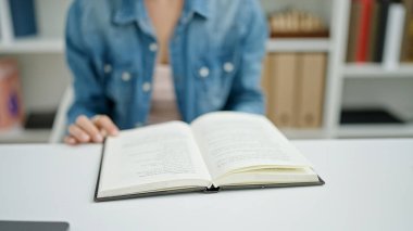 Üniversite sınıfında masa başında oturmuş kitap okuyan beyaz bir kadın.