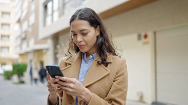 Genç ve güzel bir İspanyol kadın sokakta ciddi yüzlü akıllı telefon kullanıyor.