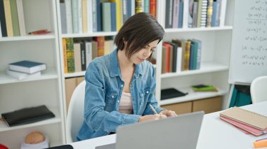 Genç beyaz kız öğrenci üniversite sınıfında dizüstü bilgisayar kullanıyor.