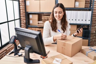 Genç ve güzel İspanyol kadın ecommerce iş işçisi. Ofisteki pakette akıllı telefon yazısını kullanıyor.