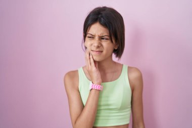 Pembe arka planda duran genç bir kız diş ağrısı ya da diş hastalığından dolayı acı dolu bir ifadeyle ağıza dokunuyor. dişçi 