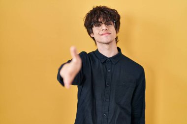 Sarı arka planda gözlük takan genç adam dostça bir selamlama ve hoş geldin hediyesi olarak tokalaşıyor. başarılı iş. 