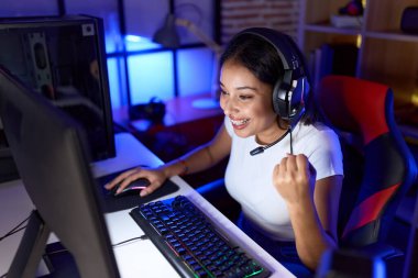 Young arab woman streamer playing video game with winner expression at gaming room