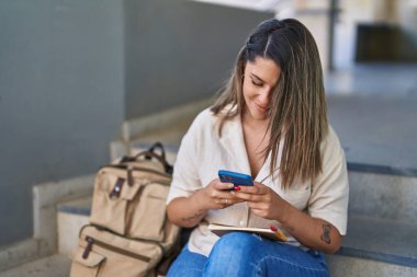Üniversitede merdivenlerde oturan, akıllı telefon kullanan genç İspanyol kız öğrenci.
