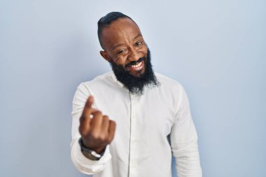 Afro-amerikan adam mavi arka planda duruyor. Buraya el kol hareketi yaparak mutlu ve gülümseyen insanları davet ediyor. 