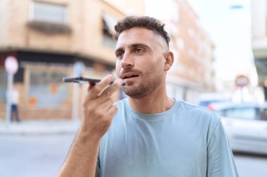 Young hispanic man talking on smartphone with serious expression at street