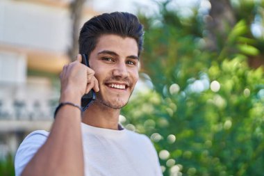 Genç İspanyol adam gülümsüyor. Parktaki akıllı telefondan konuşuyor.