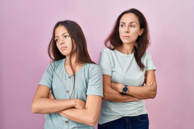 Pembe arka planda duran genç anne ve kız kollarını kavuşturmuş, ikna olmuş ve kendinden emin bir şekilde yan tarafa bakıyor. 