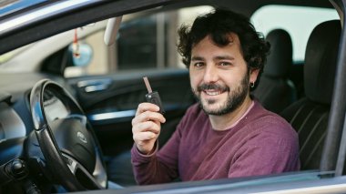 Young hispanic man smiling confident holding key of new car at street