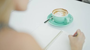 Masada oturan genç sarışın kadın kahve dükkanının terasında not alıyor.
