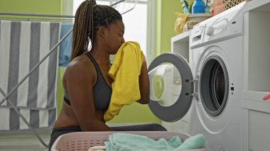 Çamaşır odasında kirli tişört kokan Afro-Amerikan kadın çamaşırları yıkıyor.
