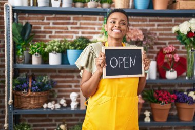 African american woman florist smiling confident holding open blackboard at florist